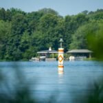 A buoy floats near green trees and buildings.